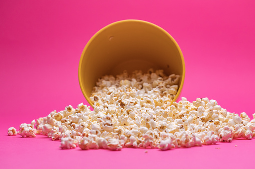 Close up shot of a spilt bowl of popcorn on a bright pink background.
