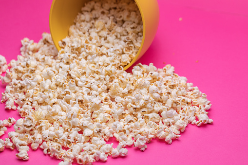 Close-up of a spilt bowl of popcorn on a bright pink background.