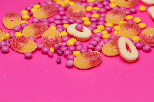 A close up shot of various candies and sweets on a bright pink background.