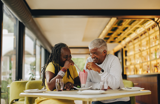 Romantic senior couple sharing a delicious strawberry milkshake in a cafe. Cheerful senior couple having a good time in a restaurant. Happy mature couple enjoying their retirement together.