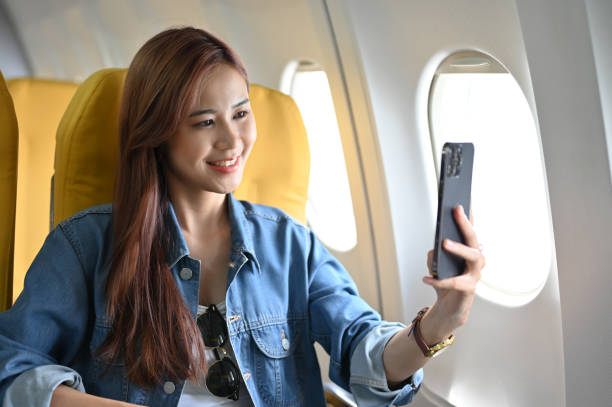 スマホを使って自撮りをしている魅力的なアジア人女性。フライト中の女性。 - commercial airplane airplane cabin passenger ストックフォトと画像