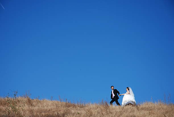 Groom walks her bride in wilted meadow on the top of a hill.