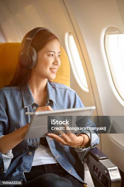 Charming Asian Woman Passenger At Window Seat With Headphones Using Portable Tablet Stock Photo - Download Image Now