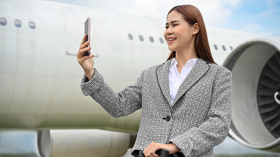 Attractive millennial asian businesswoman or female entrepreneur using a smartphone to take a picture of the view after landing from her international flight.