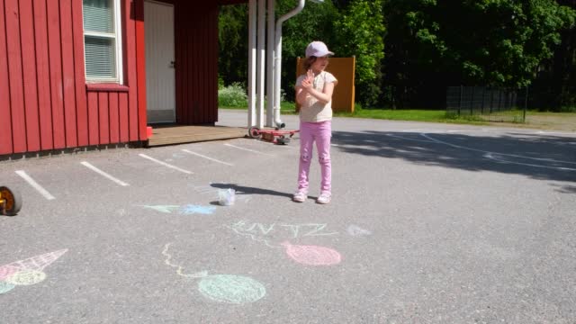 A girl, a child of 6 years old, draws with crayons on an asphalt road.