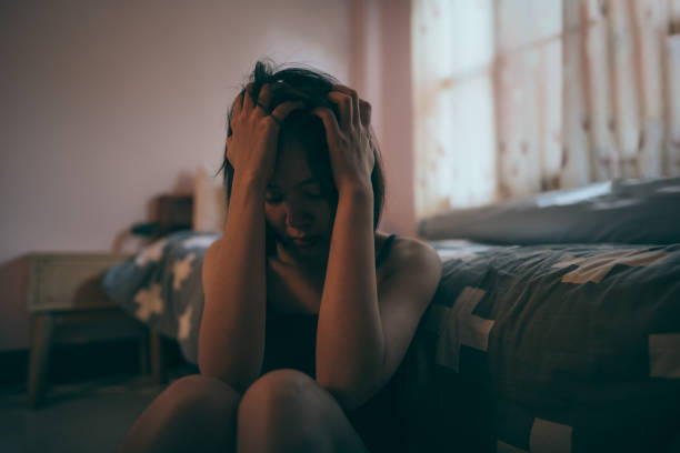 una donna depressa che si stringe la fronte in una camera da letto scarsamente illuminata. - schizophrenia foto e immagini stock