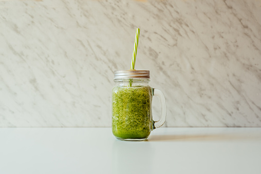 Green smoothie with apple and lemon spinach in glass jar and straw on light background,