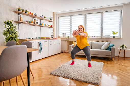 Young plus size woman exercising in the morning at home. Doing squats.