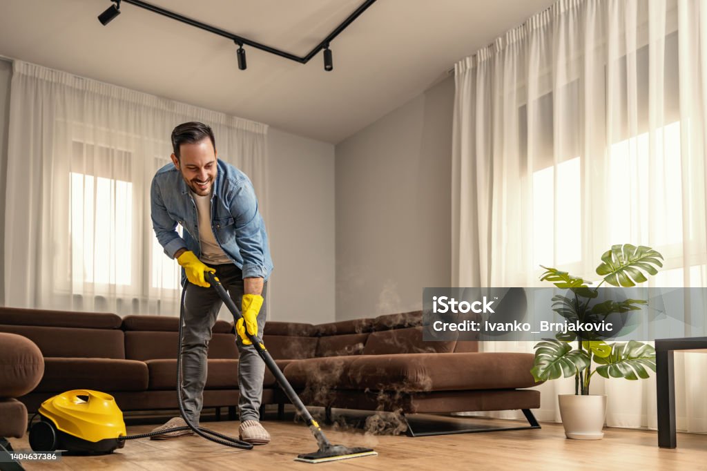 Young man using vacuum cleaner at home Man using steam vapor cleaner in living room. Steam Stock Photo