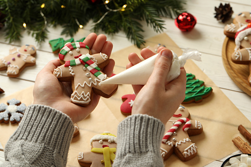 Making homemade Christmas cookies. Girl decorating gingerbread man at white wooden table, closeup