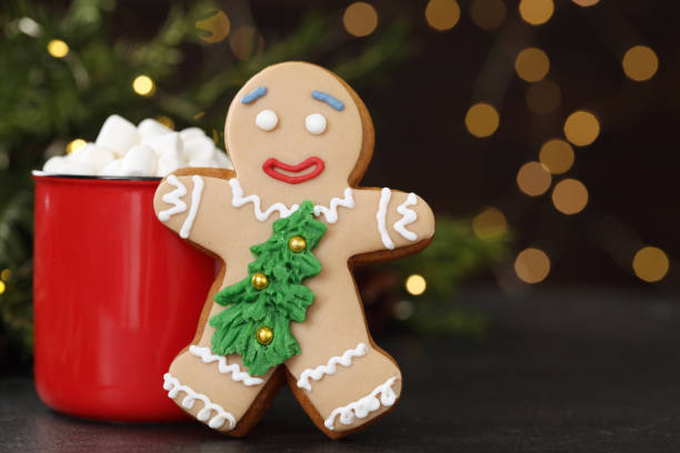 istock Gingerbread man and red cup with marshmallows on black table against blurred festive lights. Making homemade Christmas cookies 1404638777