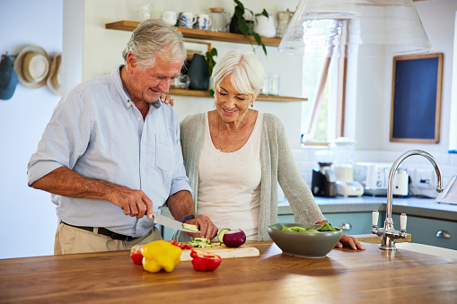 Smiling senior couple standing together at a kitchen island at home and chopping vegetables for a healthy lunch