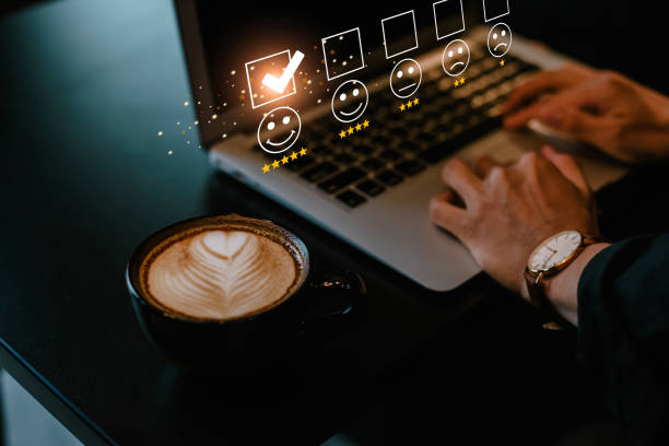 istock Man pressing face emoticon on the keyboard laptop and selecting smiley face icon and a 5 star rating in coffee shop. Demonstrates that customer satisfaction is essential to a successful business. 1404640179