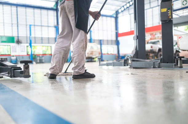 mecânico no centro de reparos automáticos limpeza usando um esfregão espremer água do piso epóxi. no centro de serviço de reparo de carros - cleaning services - fotografias e filmes do acervo