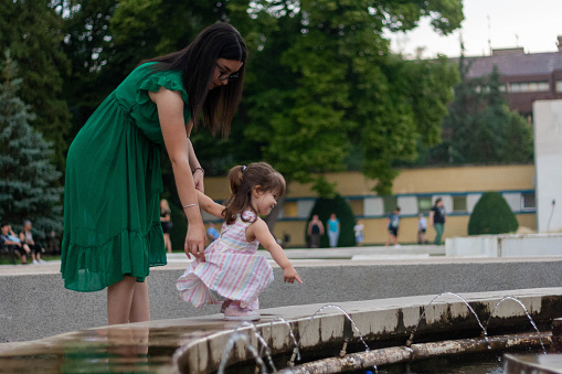 The child enjoys the time spent with the nanny. She wants to touch the water, and the woman helps her.