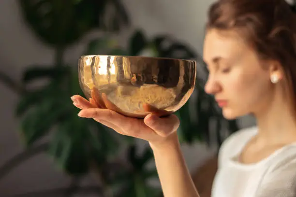 Young woman playing on a singing tibetian bowl.Relaxation and meditation.Sound therapy,alternative medicine.Buddhist healing practices.Clearing the space of negative energy.Selective focus,close up.