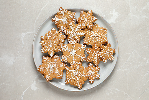 A plate filled with Christmas cookies decorated with frosting and icing for winter holiday celebrations. The baked dessert collection of sweet food features Christmas tree, gingerbread man, snowman, star, heart, and snowflake shapes against the green background of a ceramic plate. The light wooden table area allows for copy space.