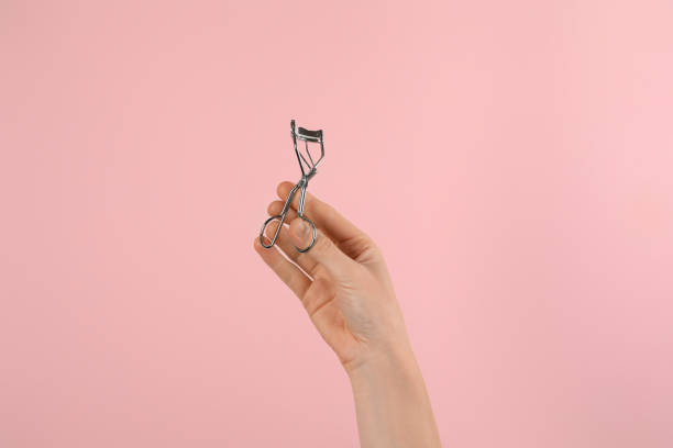 istock Woman holding eyelash curler on pink background, closeup. Makeup tool 1404642275