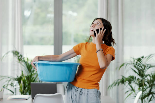 woman collecting water leaking from the ceiling - roof leak imagens e fotografias de stock