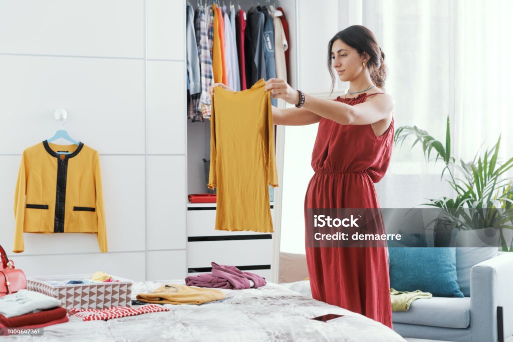 Woman choosing clothes in her bedroom Elegant woman in her bedroom, she is decluttering her wardrobe and choosing clothes Closet Stock Photo