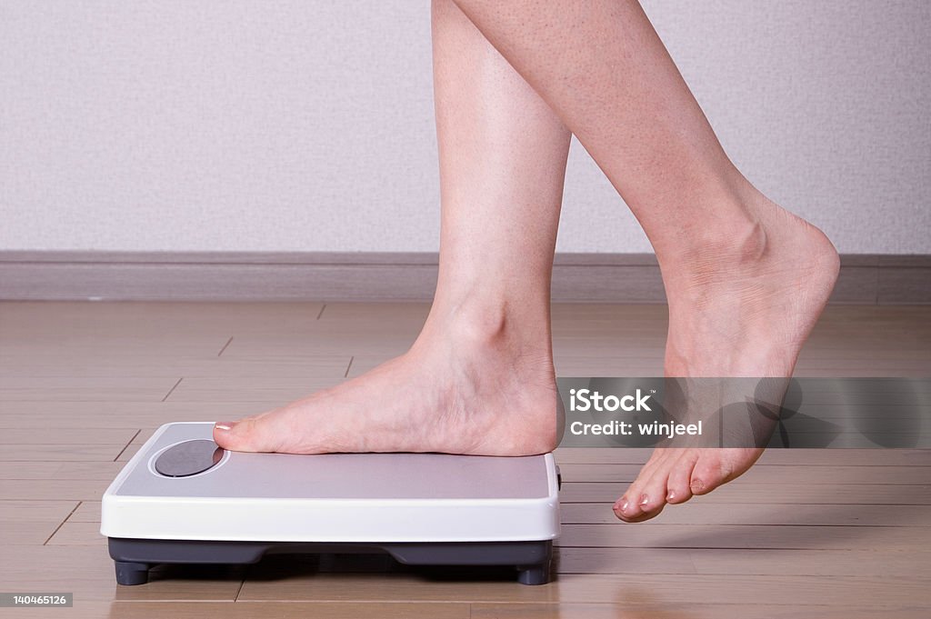 Stepping on scales Woman stepping on scales and weighing herself Adult Stock Photo