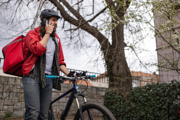 istock Male delivery person, talking on mobile phone, while pushing bicycle 1404652623