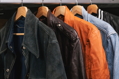 Various vintage suede leather and jeans jackets on hanger rack in a used goods store. Thrifting and sustainability in clothing concept