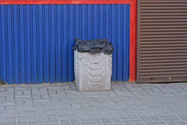 one gray concrete bin stands on the sidewalk outside against a blue and brown metal wall