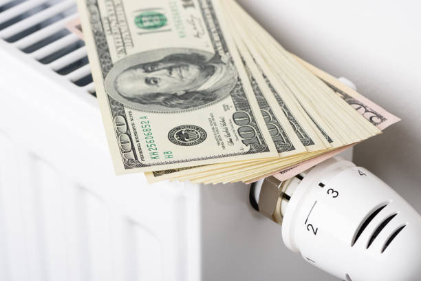 istock Stack of dollar money banknotes on heating radiator battery with thermostat temperature regulator 1404656330