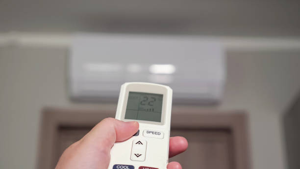 istock Hand with remote control turns on white air conditioner 1404658536