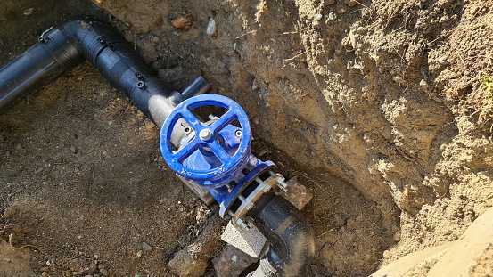 Blue faucet to control sewerage system in ground. Water pipes in trench. Water supply distribution manifold.