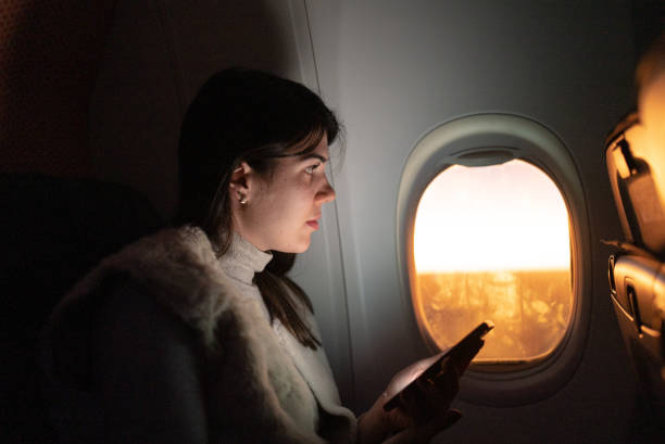 istock Woman traveling by plane and looking through window and using mobile phone 1404663898