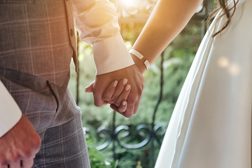 Young married couple holding hands, ceremony wedding day outdoors. Close-up hands of bride (fiancee) and groom during wedding registration. Married life and happy family concept. Copy space