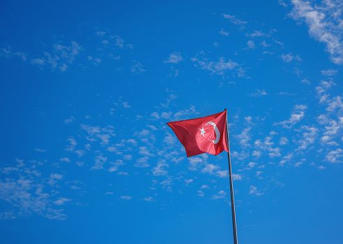 Waving Turkish Flag with blue sky in background on sunny day. Turkish national flag with white star and moon on pole.