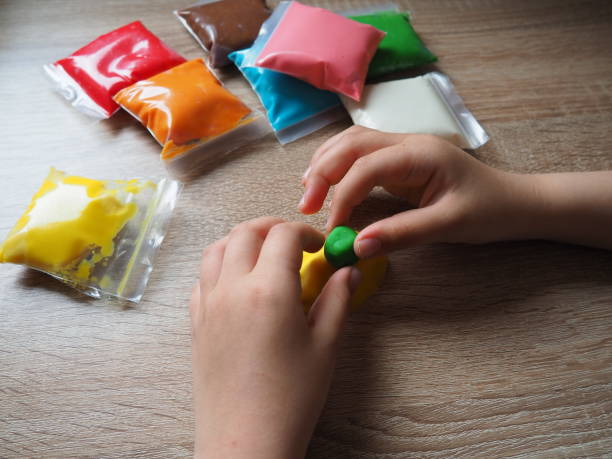 istock Children's hands crumple soft plasticine. Packages with plasticine are on the table. Creativity for the development of fine motor skills of hands. Creating a mold or model from plasticine 1404668211