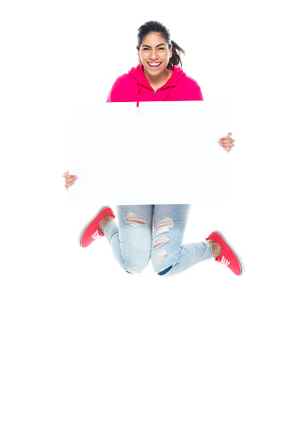 One person of aged 20-29 years old who is beautiful with black hair generation z female jumping in front of white background wearing canvas shoe who is excited who is showing with hand and holding banner sign with copy space