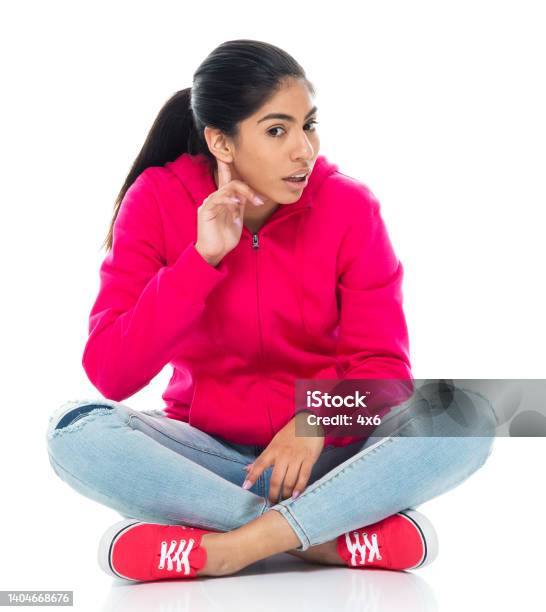 Generation Z Young Women Sitting On Floor In Front Of White Background Wearing Hooded Shirt Stock Photo - Download Image Now
