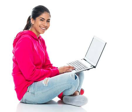 Profile view of aged 20-29 years old who is beautiful with long hair generation z young women sitting in front of white background wearing hooded shirt who is smiling who is working and using computer
