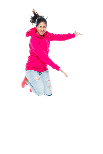 Front view of aged 20-29 years old who is beautiful with long hair generation z female jumping in front of white background wearing canvas shoe who is excited who is pointing
