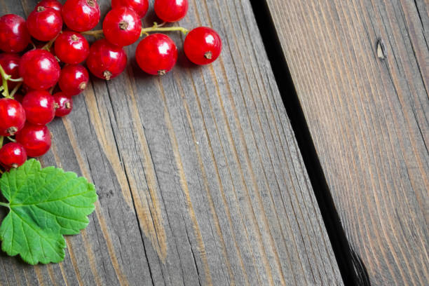 Red currant berries with a zedlen leaf lie on a wooden table. space under the inscription. In the corner of the photo lies a red currant with a leaf. Photo under the inscription.