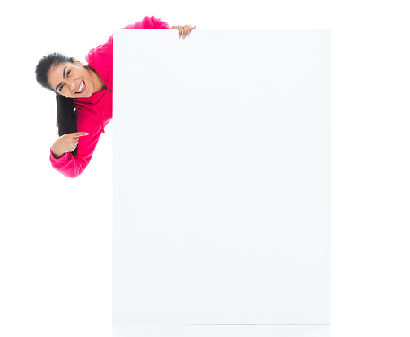 Full length of aged 20-29 years old who is beautiful with long hair generation z young women standing in front of white background wearing pants who is happy who is showing with hand and holding placard with copy space