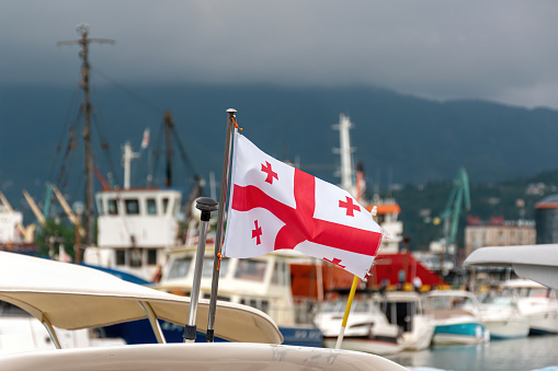 Georgian flag on a cruise yacht ship boat over blurred marine bay background