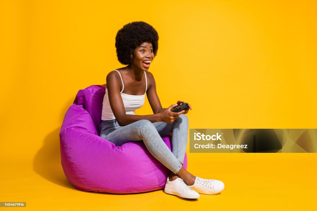 Photo of adorable attractive young lady wear casual outfit sitting beanbag enjoying playstation game isolated yellow color background Photo of adorable attractive young lady wear casual outfit sitting beanbag enjoying playstation game isolated yellow color background. One Woman Only Stock Photo