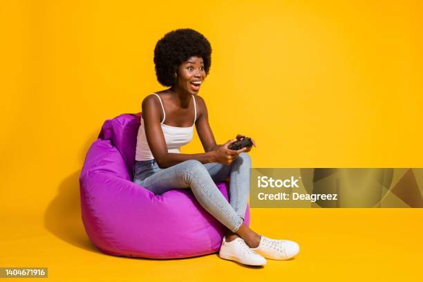 Photo Of Adorable Attractive Young Lady Wear Casual Outfit Sitting Beanbag Enjoying Playstation Game Isolated Yellow Color Background Stock Photo - Download Image Now
