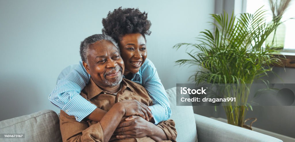 Adult daughter visits senior father in assisted living home. Adult daughter visits senior father in assisted living home. Portrait of a daughter holding her elderly father, sitting on a bed by a window in her father's room. Family Stock Photo