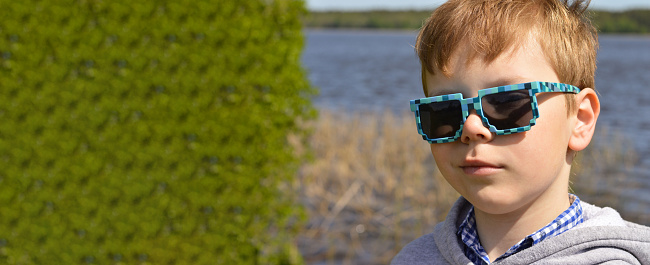 Portrait of smart little boy wearing sunglasses smirking. natural background, place for text, banner.