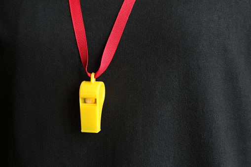 A yellow whistle with a red string hanging with the referee's shirt in flat style.