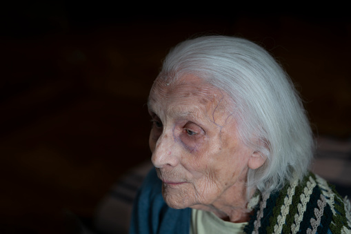 Side view of Senior, 95 years old woman, alone at home, at time of COVID-19. Dark background