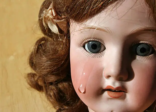 Portrait of a broken, antique porcelain doll face with tear.