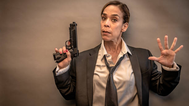 Portrait of a young woman with a pistol. She looks directly, focused and sternly at her opposite. She is ready for anything. Dark and mysterious, Film Noir style.